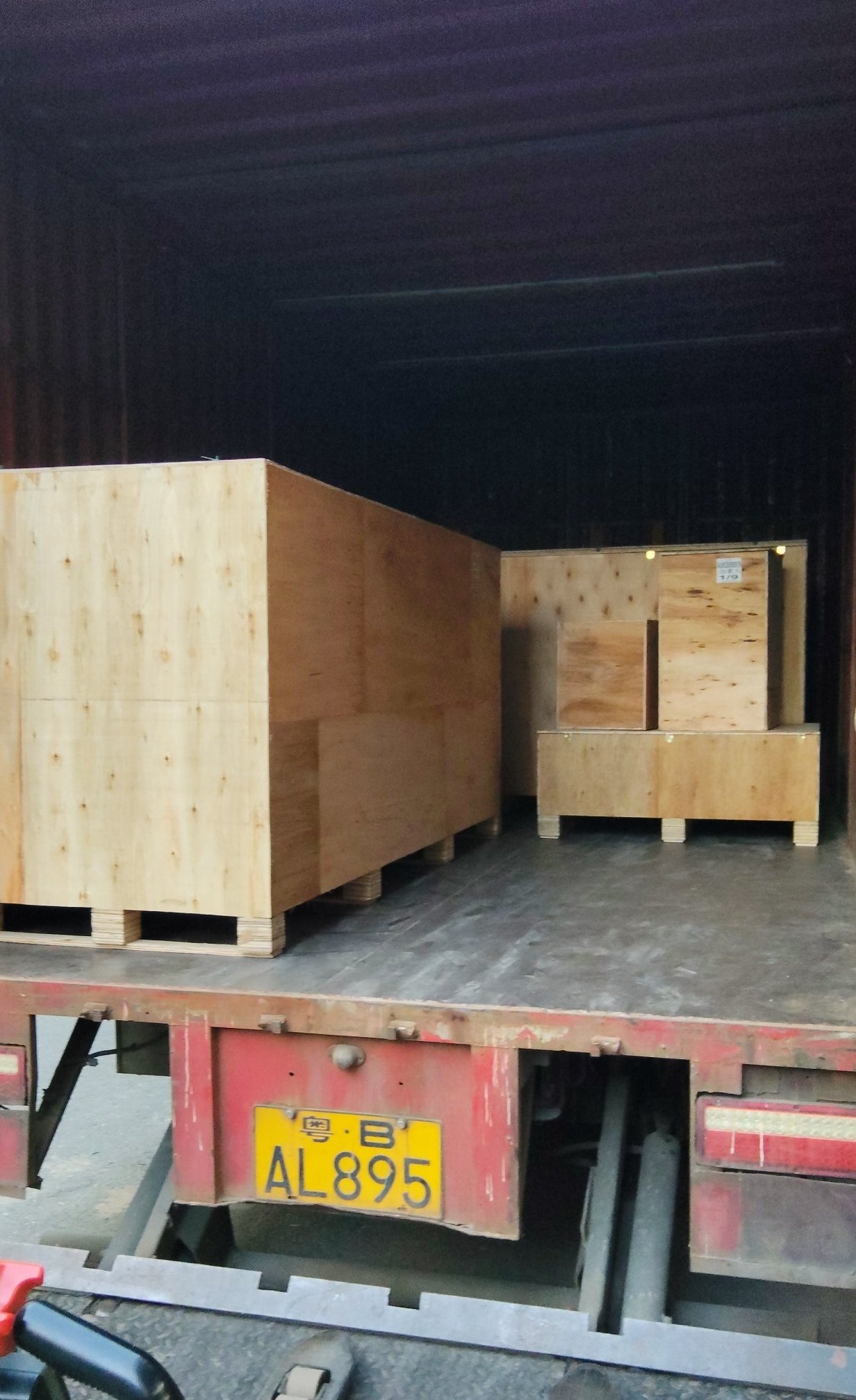 Inside a shipping container at the warehouse, showing two plywood-cased units sitting on timber bearers with strapping across them, on the trailer bed with the unit number plate on the rear doors
